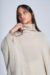 Poncho tejido color beige, con cuello alto y corte asimétrico.