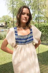 Túnica de lino color crudo con corte holgado y mangas cortas. Presenta una pechera cuadrada en el frente y la espalda confeccionada con textiles antiguos en color azul con patrones geométricos de ondas.