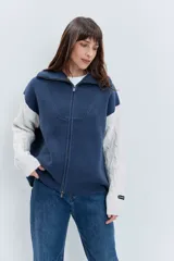 Cardigan de punto con diseño bicolor, cuerpo en color marrón y mangas largas en color crema con textura trenzada. Presenta cuello polo, cierre frontal con cremallera y puños acanalados.