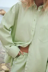 Camisa oversize de cuello solapa, manga larga con puño caído y bolsillo de plastrón en el pecho. Presenta un patrón de rayas verticales sutiles en tono verde lima.