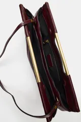 Bolso de mano de diseño estructurado en color bordó, con asa rígida dorada integrada en la parte superior y cierre magnético.