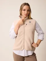 Chaleco de sherpa color beige con cierre frontal completo, cuello alto y bolsillo con cierre en el pecho que incluye un detalle circular con logo.