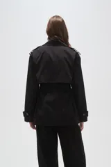 Trinchera de corte corto y diseño clásico, confeccionada en poliéster color negro. Presenta solapas amplias, cierre frontal cruzado con lazo ajustable en la cintura, charreteras en los hombros y puños con trabillas.