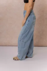 Jean de tiro alto con silueta balloon oversize, confeccionado en denim rígido de lavado celeste desgastado. Presenta costuras curvas que aportan volumen, cierre y botón frontal, y bolsillos funcionales.