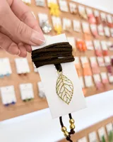 Choker con tiento de gamuza color marrón oscuro y dije de hoja calada dorada. Incluye dos cuentas doradas en el extremo del tiento.