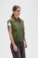 Chaleco de algodón color verde oliva, con cierre frontal y cuello de pana en color marrón. Presenta un diseño holgado con elástico en la cintura.