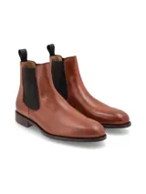 Bota tipo Chelsea de cuero color marrón, con paneles laterales elásticos en color negro y tirador en la parte trasera. Presenta una suela plana con pequeño tacón.