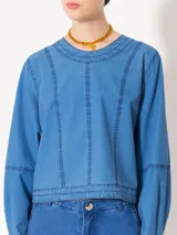Top de manga larga color azul, confeccionado en denim paper touch. Presenta cuello redondo y recortes en el frente que estilizan la silueta. Tiene cartera en la espalda con broches para facilitar el acceso.