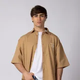 Camisa de manga corta azul oscuro de corte boxy, confeccionada en algodón. Presenta cuello camisero, cierre frontal con botones y un pequeño bordado en el pecho con las siglas 'VCP CNPT' y el número '333'.
