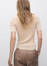 Jersey de punto fino color beige, con cuello camisero, manga corta y cierre frontal con botones pequeños. Diseño entallado de canalé.