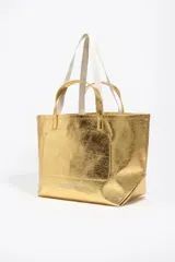 Bolso tipo tote de Bimba y Lola, color dorado con acabado metalizado y efecto arrugado. Presenta un diseño cuadrado con estampado central de la marca en un recuadro oscuro y doble asa de mano en color crema.