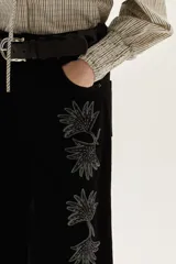 Jean de corte pata ancha color negro, con diseño de paneles frontales y bordados florales a lo largo de las piernas.