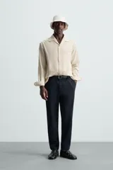 Pantalón chino de algodón color crema, corte regular fit, con cierre frontal de cremallera y botón, bolsillos delanteros y bolsillos traseros de vivo con botón.