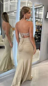 Vestido largo strapless de color dorado con acabado brillante, de corte ajustado y diseño drapeado en el torso.