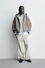 Cazadora boxy fit de algodón con estampado de cuadros en tonos beige y gris. Presenta cuello con capucha, cierre frontal de cremallera, mangas largas con puños elásticos y bolsillos frontales tipo canguro.