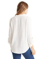 Blusa de color blanco con escote en V y cuello mao. Presenta mangas largas con presilla y botón para regular el largo, y un corte holgado con ruedo redondeado.
