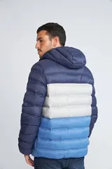 Campera puffer con diseño color block en tonos azul marino, gris y azul claro. Cuenta con capucha, cierre frontal completo, bolsillos laterales con cierre y logo estampado en el pecho.