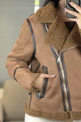 Campera tipo gamulán de color crema con interior y cuello de corderito sintético. Presenta cierre frontal cruzado, bolsillos laterales con cierre y detalles de costuras en contraste color marrón oscuro.