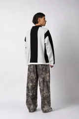 Sweater de punto con diseño a rayas verticales en color beige y blanco, de corte holgado y cuello polo abierto. Presenta un logo bordado en el centro del pecho.