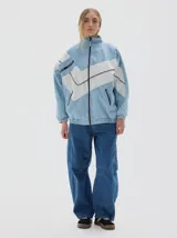 Campera de jean estilo deportivo con cierre frontal, cuello alto y diseño de paneles en forma de V en color blanco. Presenta corte oversized, puños y cintura elásticos, y bolsillos frontales con cierre.