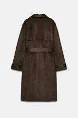 Trench largo de ante sintético color marrón oscuro, de corte cruzado con doble botonadura, solapas amplias y cinturón ajustable del mismo tejido. Cuenta con bolsillos laterales de vivo, mangas largas con trabillas en los puños y detalles en los hombros.