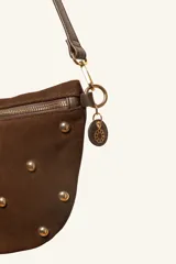 Bandolera de gamuza color marrón con diseño de media luna, decorada con tachas metálicas doradas distribuidas en el frente. Cuenta con cierre superior metálico y correa larga ajustable para llevar cruzada.