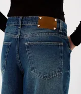 Pantalón de jean con corte super wide leg y tiro medio. Presenta un lavado uniforme con efecto levemente marcado, cintura con pasantes, cierre frontal con botón y cremallera, y bolsillos funcionales. Incluye remaches metálicos decorativos en forma de corazón.