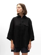 Camisa de lino con mangas tres cuartos, cuello clásico, cierre frontal con botones y un bolsillo en el pecho izquierdo. Presenta un diseño holgado con un pliegue en la espalda.