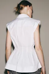 Camisa blanca de cuello solapa y sin mangas, con bajo acabado en peplum y cierre frontal con botones ocultos.