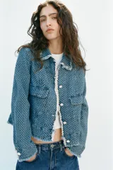 Chaqueta de denim de corte clásico con textura perforada, cuello solapa, bolsillos delanteros de plastrón, cierre frontal con botones a contraste y detalles de flecos en los bordes.