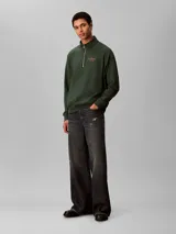 Buzo Calvin Klein de felpa color verde oscuro, con cuello alto, cierre frontal parcial de un cuarto y manga larga. Presenta el logo de la marca bordado en el pecho.