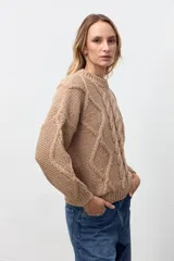 Sweater de punto color camel con cuello redondo y diseño de trenzas verticales en el frente y mangas. Presenta puños y ruedo acanalados.