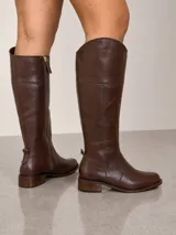 Bota de caña alta estilo montar, confeccionada en cuero marrón. Presenta punta redonda, taco bajo cuadrado y cierre lateral completo.