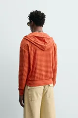 Sudadera con capucha de corte relajado, confeccionada en tejido a rayas horizontales en tonos naranja. Cuenta con cierre frontal de cremallera, cordones ajustables en la capucha y puños y ruedo en rib.