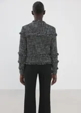 Chaqueta de tweed en tejido jaspeado negro y blanco, con diseño recto, cuello redondo, manga larga y cierre delantero con botones. Presenta terminaciones deshilachadas y detalles de flecos.