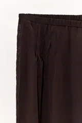 Pantalón bombacho de color marrón oscuro, confeccionado en lyocell 100%. Presenta tiro medio con cintura elástica, pliegues frontales, detalle de encaje a tono en el lateral y bajo abullonado con elástico.
