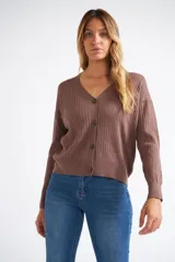 Cárdigan de tejido liviano con textura acanalada, cuello en V y cierre frontal con botones. Presenta mangas largas y un diseño clásico con detalle de grifa en cuero.