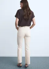 Jeans de tiro medio y corte recto de color marfil, con diseño crop y bajo deshilachado. Presenta cinco bolsillos, trabillas para cinturón y cierre frontal con cremallera y botón metálico.