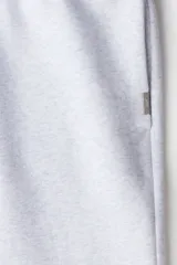 Pantalón deportivo de tejido de felpa color gris melange, con interior cepillado suave. Presenta cintura elástica con cordón de ajuste oculto, bolsillos laterales y un bolsillo trasero abierto. Las piernas terminan en puños acanalados.