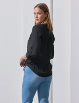 Blusa blanca de gasa marca Zac & Rachel, con cuello a la base, escote en V, abertura central con botones, bolsillo aplicado en el pecho y mangas largas regulables con presilla y botón. Tiene terminación opcional de nudo en el ruedo.