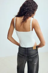Body negro con aros, escote en pico y detalles de encaje a tono en las copas y en el borde de las piernas. Cuenta con tirantes anchos y cierre inferior con botones a presión.