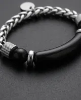 Pulsera masculina compuesta por una barra central de piedra onix negra, flanqueada por piezas de acero con textura grabada y esferas metálicas. Diseño elegante y moderno con cierre ajustable.