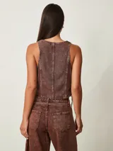 Top estilo chaleco crop de denim marrón con efecto acid wash, escote en V, cierre frontal con botones metálicos y cordones ajustables en los laterales.