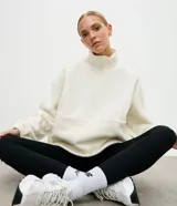 Buzo deportivo de fleece color crema, con cuello alto y cierre frontal parcial. Presenta mangas largas con puños elásticos y un diseño holgado con recortes frontales.