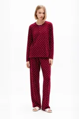 Pijama bordó con estampado de lunares blancos, compuesto por una remera de manga larga con cuello redondo y botones frontales y un pantalón largo de corte recto con cintura elástica.