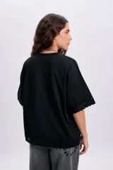 Remera negra de manga corta con detalles de encaje en el ruedo y las terminaciones de las mangas, de corte holgado y cuello redondo.