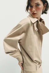 Vestido corto de cuello solapa y manga larga, con bolsillos delanteros y detalle de cinturón a tono. Presenta cierre frontal con cremallera oculta y bajo con aberturas laterales.