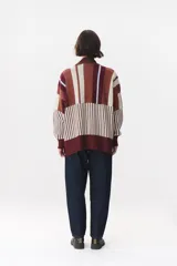 Buzo oversize de tejido de punto con diseño de bloques y rayas verticales en colores rojo, verde, bordó y crema. Presenta cuello alto tejido y terminaciones en rib en puños y ruedo.
