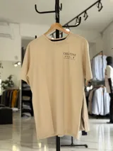 Remera oversize color beige, con diseño estampado en la espalda que incluye tipografía grande y texto descriptivo en negro.