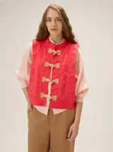 Chaleco rojo de lino y algodón con cuello mao y cierre frontal con alamares de cuero y cordón. Presenta bolsillos aplicados en los laterales y costuras pespunteadas a contratono.